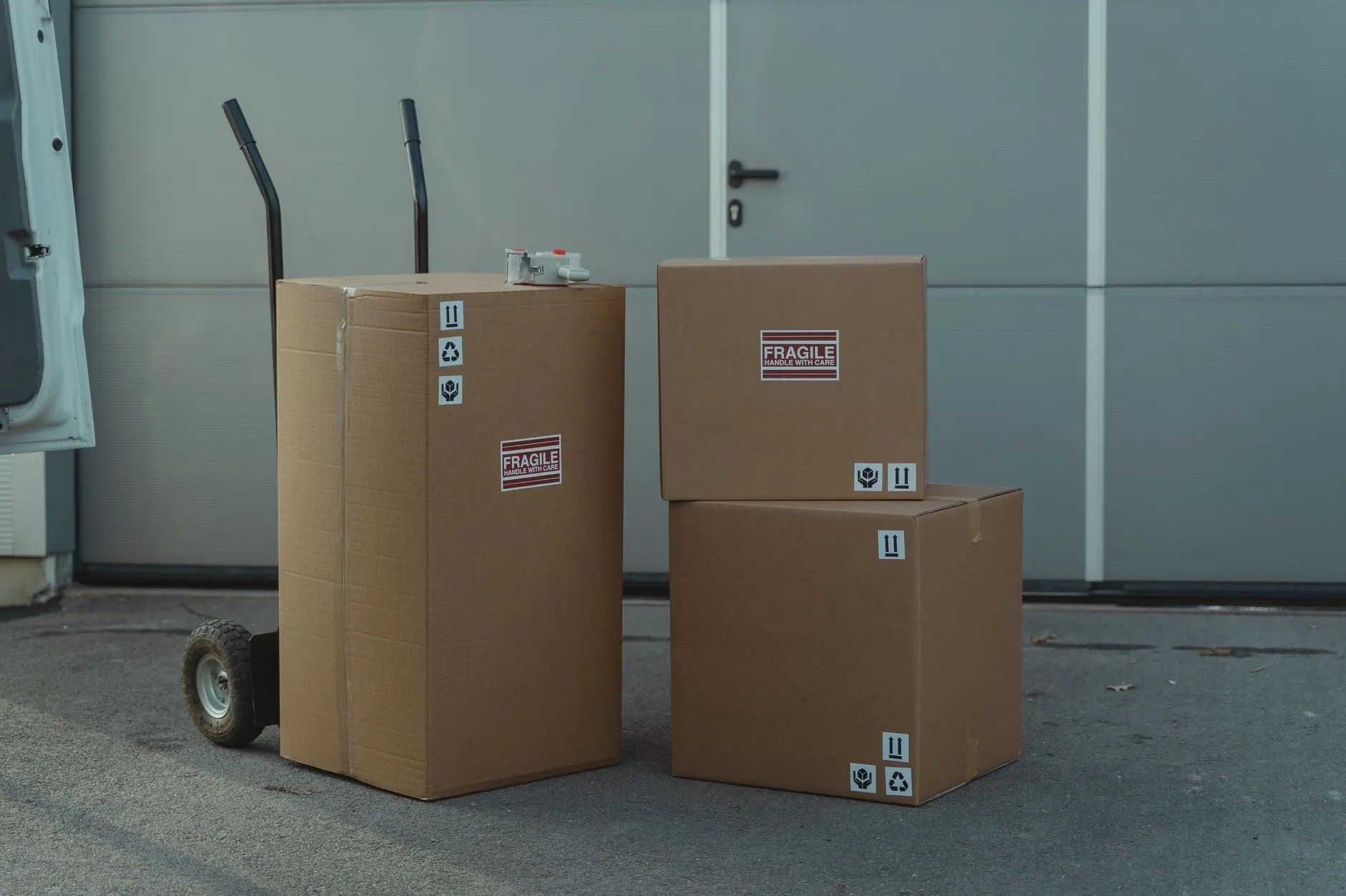 A mover wheeling a stack of boxes on a hand truck towards an open van