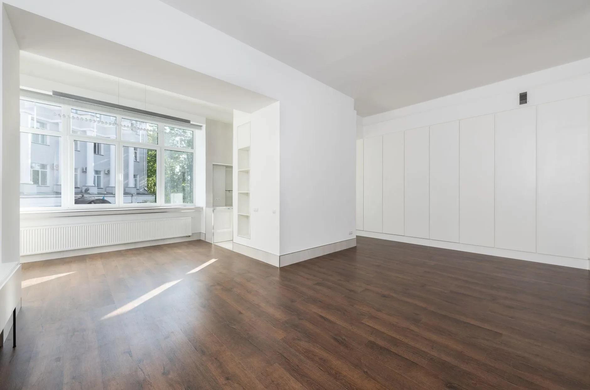 A bright, empty room with pale floorboards and a tall window