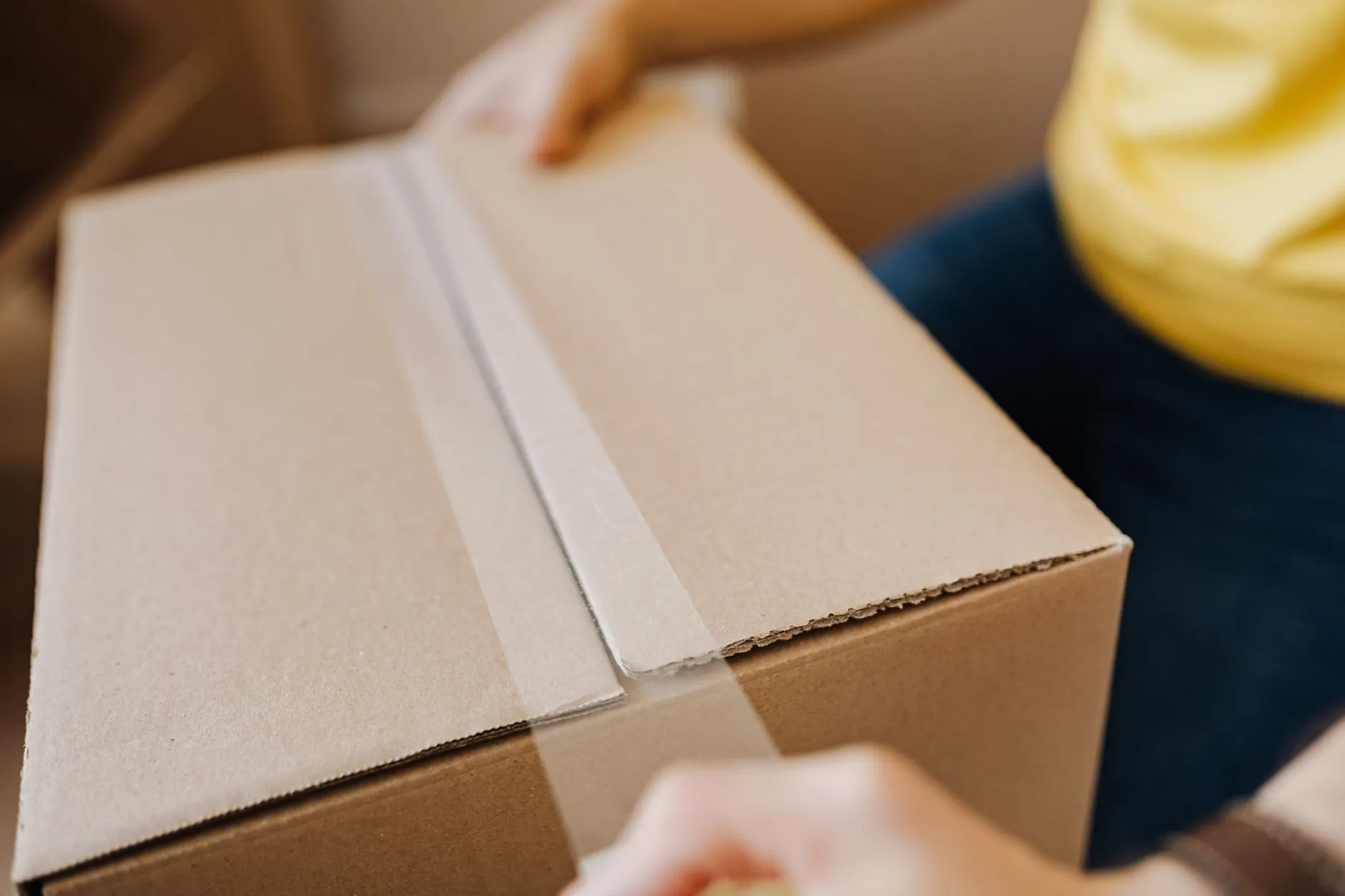 Hands taping the seam of a plain cardboard box