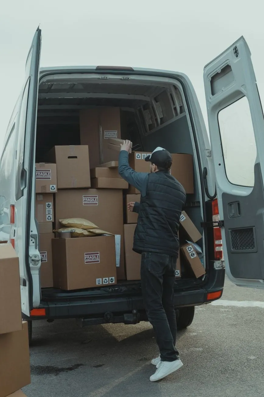 A mover, seen from behind, stacking boxes into the back of a white van