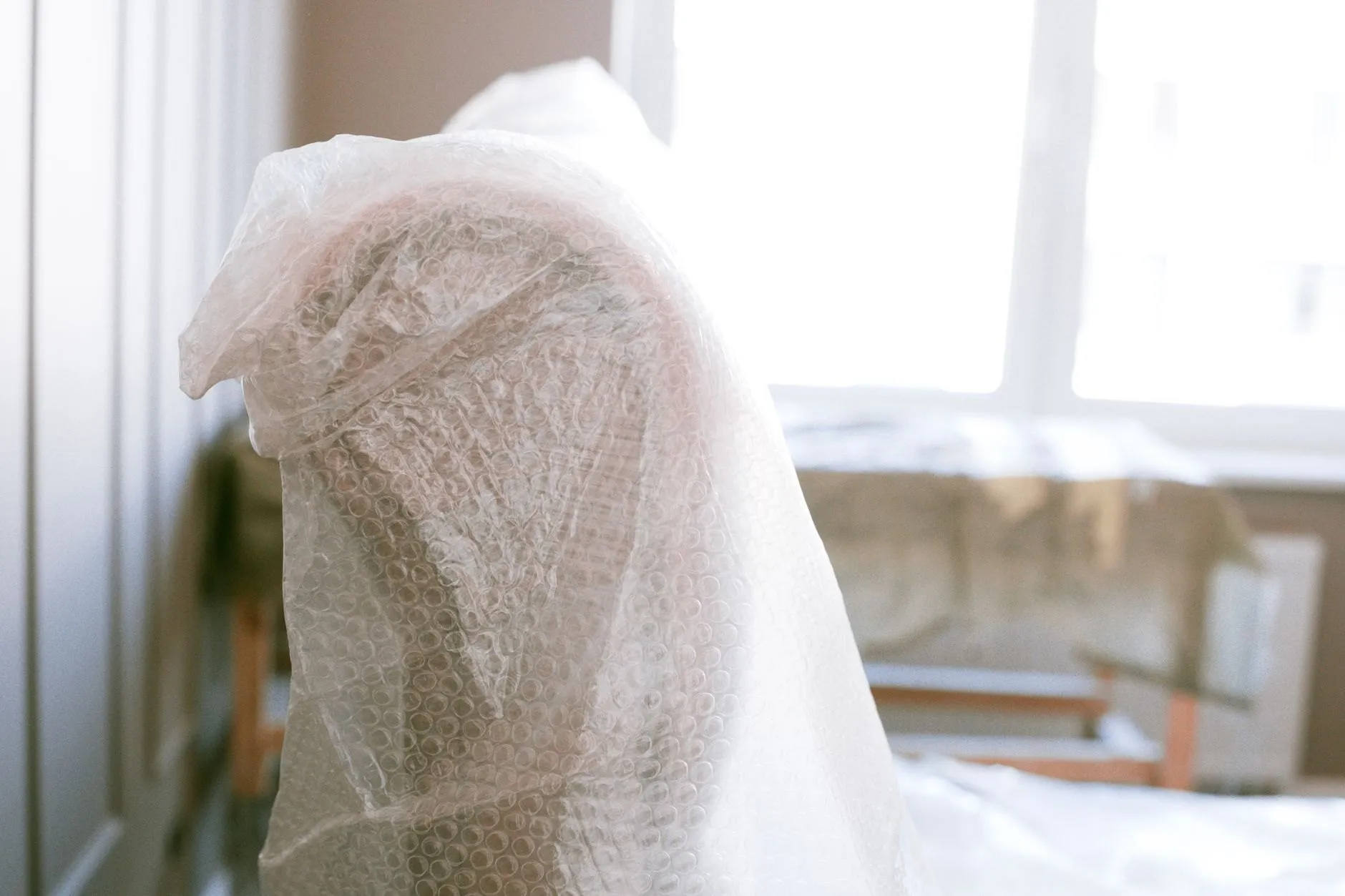 A chair wrapped in bubble wrap by a bright window, ready to move